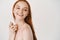 Close-up of pale redhead woman standing naked on white background, turn right and smiling at copy space about skincare