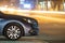 Close up of parked car on roadside at night with blurred view of traffic lights of moving vehicles on city street