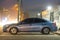 Close up of parked car on roadside at night with blurred view of traffic lights of moving vehicles on city street