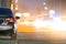 Close up of parked car on roadside at night with blurred view of traffic lights of moving vehicles on city street