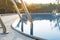 Close-up of a part of swimming pool with a stainless steel ladder and blue water on sunset. Summer vacation, holidays, relax