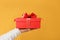 Close-up partial view of man in sweater holding red gift box on yellow background.Gift giving concept