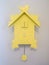 Close up of pastel yellow wooden cuckoo clock mounted on gray interior wall