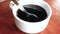 Close-up of person hand stirring black coffee with spoon in a white cup on wooden table background.