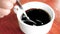 Close-up of person hand stirring black coffee with spoon in a white cup on wooden table background.