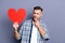 Close up photo attractive he him his guy arms hands large red paper heart not sure agree celebration valentine day hate