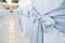 Close-up photo of big blue bows tied on white wedding chairs.