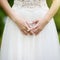 Close-up photo of bride`s hands with golden engagement ring on beautiful white wedding dress