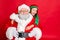 Close up photo of charming santa claus in eyeglasses eyewear and his little elf helper in green hat headwear hugging