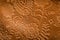 Close up photo of embossed leather with a floral design in rust brown.