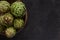 Close up photo of fresh artichoke in the old wooden bowl. Top view on dark background