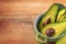 Close-up photo of fresh sliced avocados, brown seeds visible in green bowl on brown wooden background.