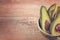 Close-up photo of fresh sliced avocados, brown seeds visible in green bowl on brown wooden background. Vegetarian food concept.