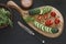 Close-up photo of fresh vegetables on wooden cutting board with knife on black concreted table background.