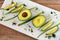 Close-up photo of fresh whole avocados and fresh onion in white porcelain dish on brown wooden background.