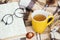 Close up photo of glasses, yellow mug with tea, book and orange fallen leaves on beige plaid on outside. Comfort and
