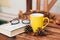 Close up photo of glasses, yellow mug with tea, pine cone, book and orange fallen leaves on wooden table outside