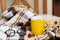 Close up photo of glasses, yellow mug with tea, pine cones, book and orange fallen leaves on beige plaid on outside