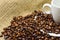 Close-up photo of grains of roasted black coffee with white porcelain cup on jute bags with blurred background