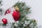 Close-up photo of a large red Christmas toy in the form of a ball and small one on a branch of a coniferous tree lying in the snow