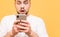 Close-up photo, shocked man looking at a smartphone. Amazed man with a beard looking at a smartphone on a yellow background,