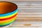 Close-up photo of a striped bowl, colored in red, blue, yellow, orange and green, on a wooden background; copy space