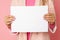 Close-up Photo, unrecognizable woman holding blank sheet of paper for commercial inscription. pink background. studio