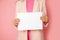 Close-up Photo, unrecognizable woman holding blank sheet of paper for commercial inscription. pink background. studio