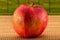 Close-up photo of wet red apple with water drops on blurred bamboo background