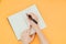 Close-up photo of a woman`s hand writing a to-do list in a clean notebook on an orange background