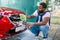 Close up photo of young African man cleaning radiator grille of luxury red car with foam and green brush mitten. Carwash