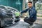 Close up photo of young Caucasian man cleaning hood of luxury electric car with foam and green brush mitten. Carwash and