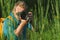 Close-up, the photographer holds a professional photo-video camera in his hands. Against the background of green beautiful nature