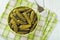 Close-up of pickled cornichons in a ceramic bowl on a green checkered napkin over table. Whole gherkins marinated with dill and