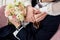 Close up picture of female and male hands with wedding rings holding together. Bride and groom holding delicate roses flower