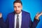 Close up picture of young handsome business man over blue isolated background clueless and confused expression with arms and hands