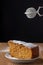 Close-up of piece of carrot cake with strainer to pour icing sugar on wooden table and black background