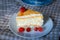 Close-up of a piece of classic cheesecake cake on a white dish and a checkered linen napkin