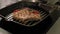 Close-up of a piece of meat on a bone being fried on a grill pan in a kitchen.