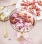 Close up of pink champagne glass with petals and pomegranate seeds on table with golden forks, cheese and plate. Elegant food and