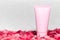 Close-up of pink cosmetic tube with mockup standing on coral flower petals. Background of grey textured wall.