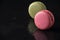 Close-up of pink and green macaron, with selective focus, on wet slate stone, with reflection,