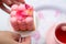 Close up pink neo cube ball velours mousse cake dessert with petals and butterfly on plate in hands near cup of tea