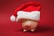 Close up of pink piggy money bank with Christmas hat on bright red background. Money accumulation, investment