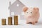 Close up of pink piggy money bank stacks of golden coins on white wall background with house. Money accumulation