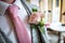 Close up of pink rose wedding boutonniere with green leaves and stalk on grooms suit jacket with matching tie colour looking smart