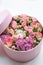 Close up of pink round box with golden ring inside decorated with purple,green,beige flowers roses on white background