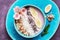 Close-up of pink yogurt with banana, almonds, chia seeds, coconut flakes in a blue bowl decorated with alstroemeria flowers.