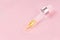 Close up of pipette with pouring liquid essential oil on pink background.