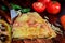 Close-up pizza slice with ham, salami and mozzarella cheese on wooden traditional background surrounded by fresh vegetables